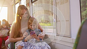 Woman and daughter using mobile phone internet social network application, traveling by bus or tram