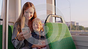 Woman and daughter using mobile phone internet social network application, traveling by bus or tram