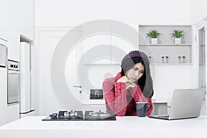 Woman daydreaming with laptop in the kitchen