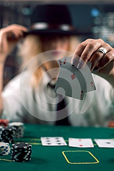Woman dealer in hat with playing cards and poker chips in casino watching the game