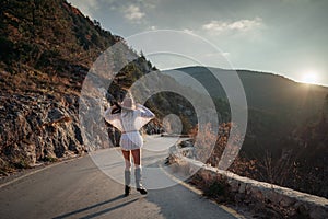 The woman is dear to the mountains. A woman in a white sweater, black boots and a hat walks along a winding alpine path