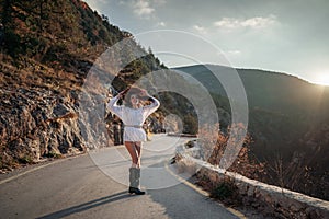 The woman is dear to the mountains. A woman in a white sweater, black boots and a hat walks along a winding alpine path