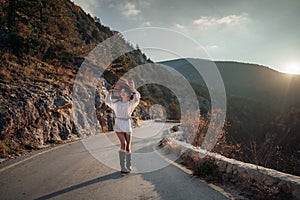 The woman is dear to the mountains. A woman in a white sweater, black boots and a hat walks along a winding alpine path