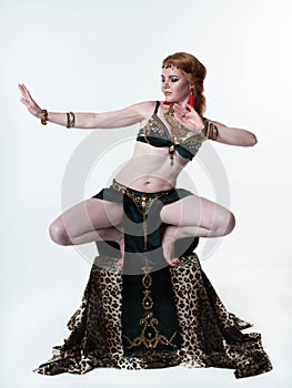 Woman in decorated traditional green belly costume with top and skirt dancing on pedestal with leopard print and looking down