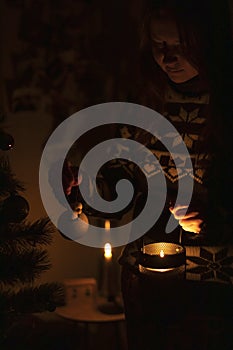 Woman decorates a Christmas tree in the dark with a candle