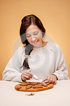 Woman on decorates a gingerbread with white frosting from a tube.