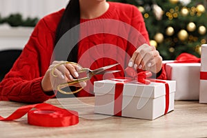 Woman decorating Christmas gift box at wooden table indoors, closeup