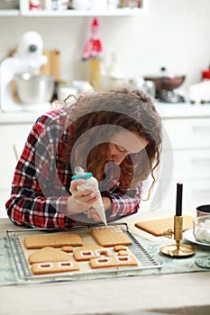 Woman is decorating christmas gingerbread cookies with icing on table with candle and ornaments. Close up. Making