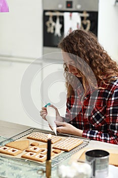 Woman is decorating christmas gingerbread cookies with icing on table with candle and ornaments. Close up. Making