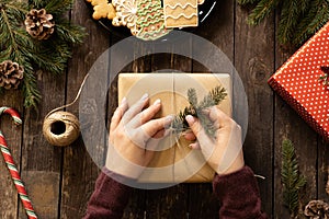 Woman decorating a Christmas present with conifer evergreen branch on a wooden table background