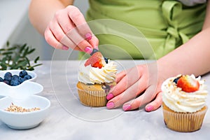 Woman decorating cupcakes in kitchen. Professional confectioner decorating top of cupcake with strawberry. Homemade pastry