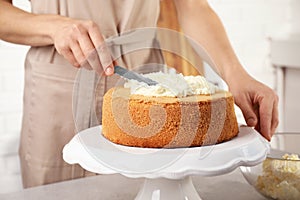 Woman decorating delicious cake with fresh cream at table indoors. Homemade pastry