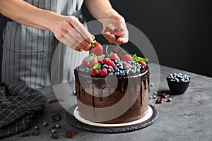 Woman decorating delicious chocolate cake with strawberries at table, closeup photo