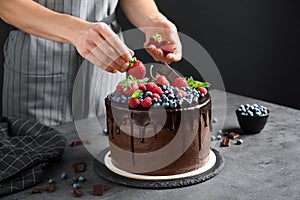 Woman decorating delicious chocolate cake with strawberries at table, closeup