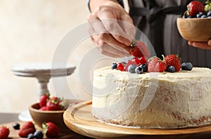 Woman decorating delicious homemade cake with fresh berries at table indoors