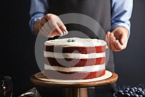 Woman decorating delicious homemade red velvet cake with blueberries