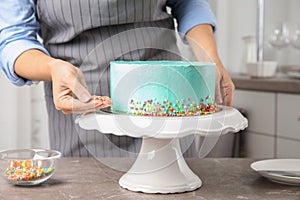 Woman decorating fresh delicious birthday cake in kitchen