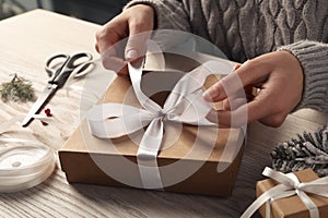 Woman decorating gift box at white wooden table, closeup. Christmas present