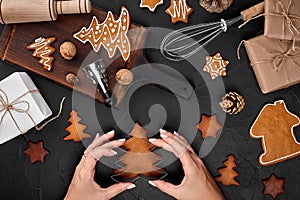 Woman decorating gingerbread Christmas cookies with icing sugar. Christmas preparations concept. Top view with copy