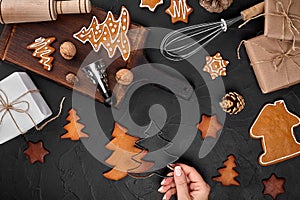 Woman decorating gingerbread Christmas cookies with icing sugar. Christmas preparations concept. Top view with copy