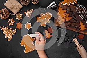 Woman decorating gingerbread Christmas cookies with icing sugar. Christmas preparations concept. Top view with copy