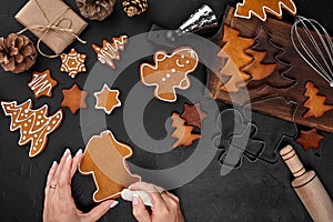 Woman decorating gingerbread Christmas cookies with icing sugar. Christmas preparations concept. Top view with copy