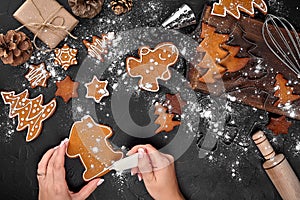 Woman decorating gingerbread Christmas cookies with icing sugar. Christmas preparations concept. Top view with copy