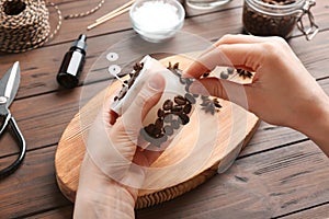 Woman decorating handmade candle with coffee beans at wooden table