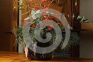 Woman decorating home interior with Christmas flower arrangement in vase.