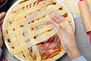 Woman decorating raw apple pie at grey table, top view