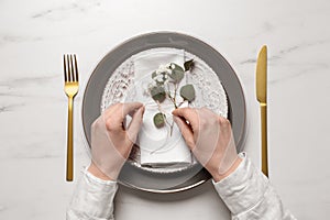 Woman decorating setting with eucalyptus leaves at white marble table, top view