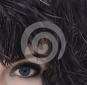 Woman with deep blue eyes in black feather headdress. Smoky eyes make-up.