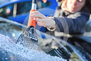 Woman deicing car windshield with ice scraper