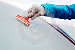 Woman deicing front car windshield with scraper