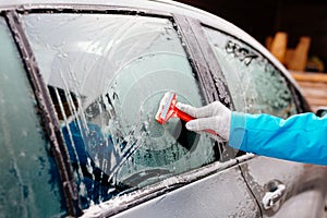 Woman deicing side car windshield with scraper