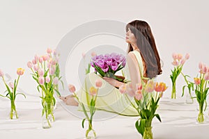 a woman in a delicate dress sits on the floor with bouquet surrounded by tulips