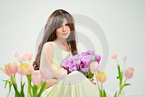 a woman in a delicate dress sits on the floor with bouquet surrounded by tulips