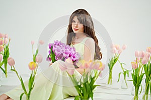a woman in a delicate dress sits on the floor with bouquet surrounded by tulips