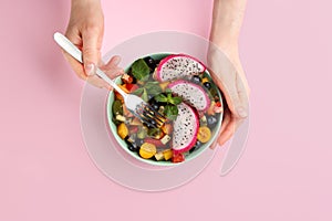 Woman with delicious exotic fruit salad on pink background, top view