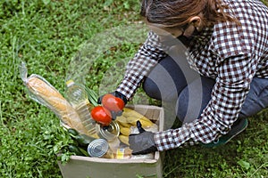 Woman delivering donations box with food during Covid 19 outbreak.Feme volunteer collects food in a box standing on the grass