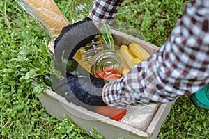 Woman delivering donations box with food during Covid 19 outbreak.Feme volunteer collects food in a box standing on the grass photo