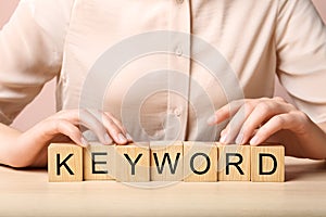 Woman demonstrating cubes with word KEYWORDS at wooden table, closeup