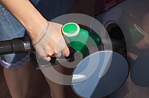 A woman in denim blue shorts with a fuelling nozzle pouring gasoline into the tank of the car at the filling station