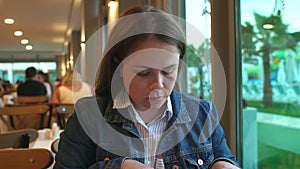 A woman in a denim jacket eating in a restaurant , she holds a knife and fork.