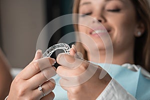 A woman in a dental clinic looks at a mouth guard close-up. Veneer as a modern and effective tool for straightening and