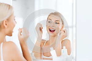 Woman with dental floss cleaning teeth at bathroom