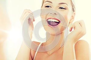 Woman with dental floss cleaning teeth at bathroom