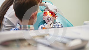 Woman dentist drives a tool in the mouth of a patient boy. The boy`s brother is standing nearby.