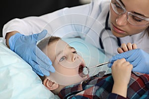 Woman dentist examines child`s teeth with metal tools