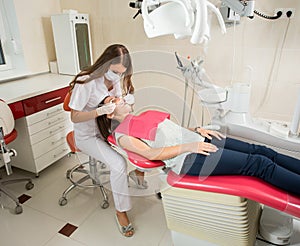 Woman dentist in her office treating female patient